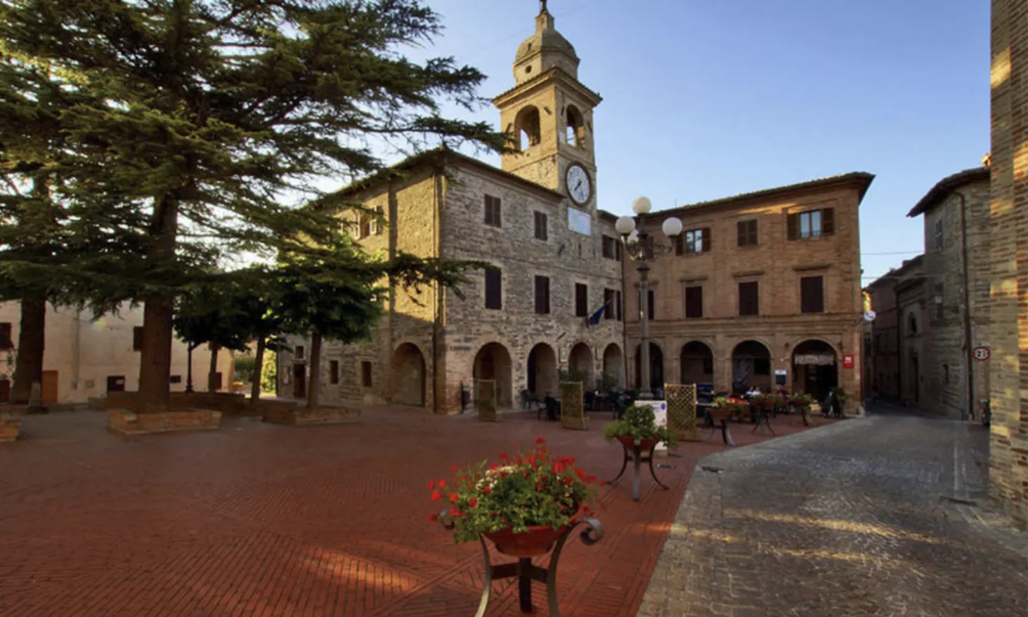 Piazza storica con torre campanaria e palazzi in pietra sede del MIDAC nelle Marche