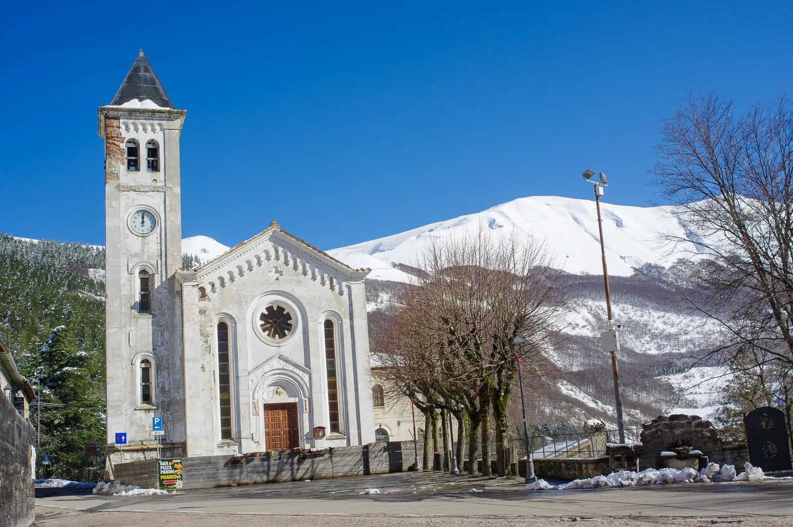 Chiesa di Bolognola con campanile e montagne innevate dei Monti Sibillini sullo sfondo