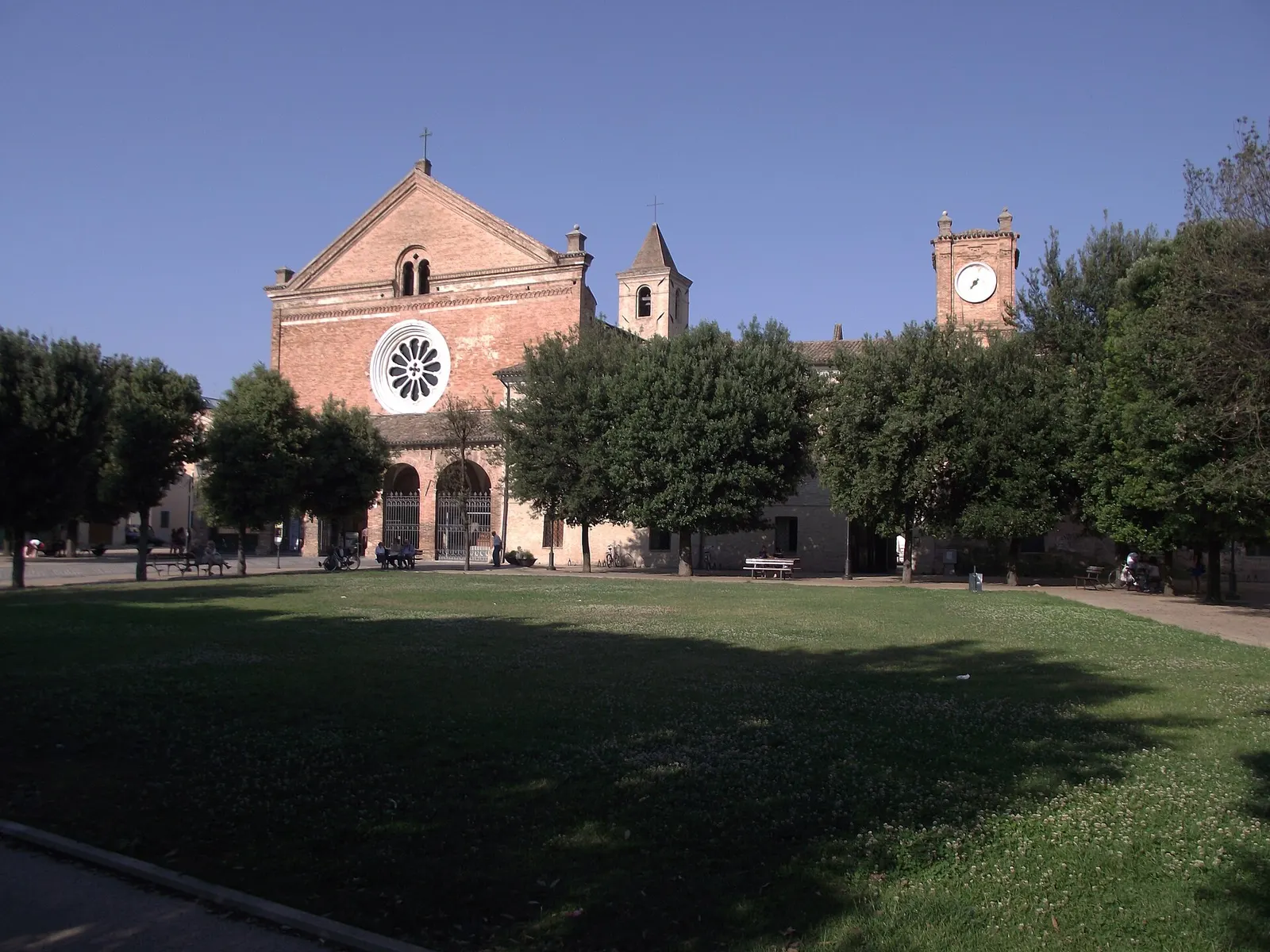 Chiesa abbaziale in mattoni rossi con rosone e piazza alberata nel centro storico di Chiaravalle
