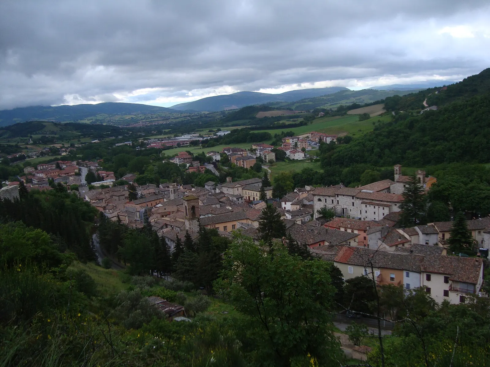 Veduta aerea del centro storico di Esanatoglia circondato da colline verdi e montagne dell'Appennino marchigiano