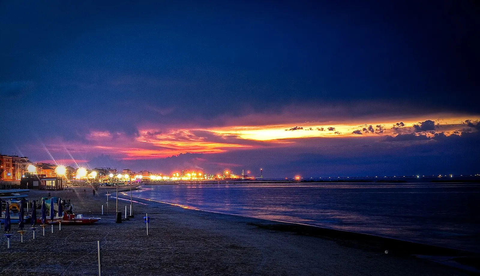Tramonto sul litorale adriatico di Falconara Marittima con spiaggia illuminata e luci della città costiera