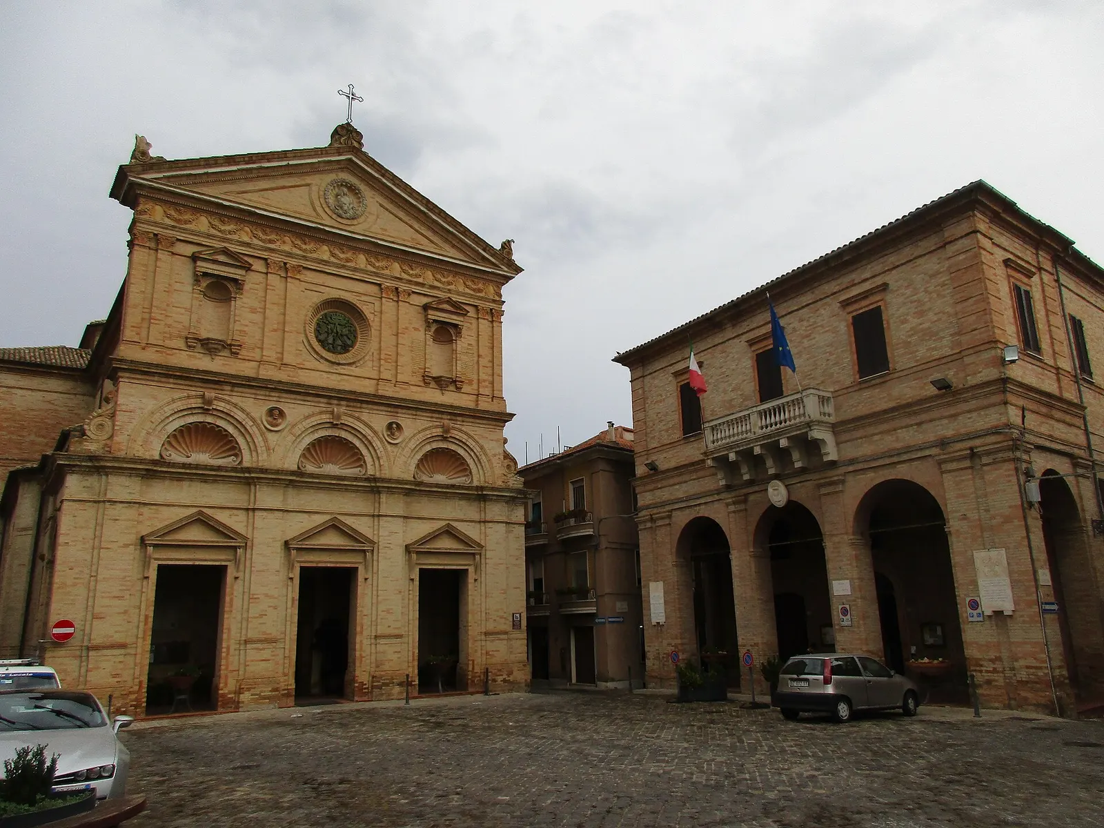 Piazza centrale di Monte Urano con chiesa storica in laterizio e palazzo comunale con portici ad archi