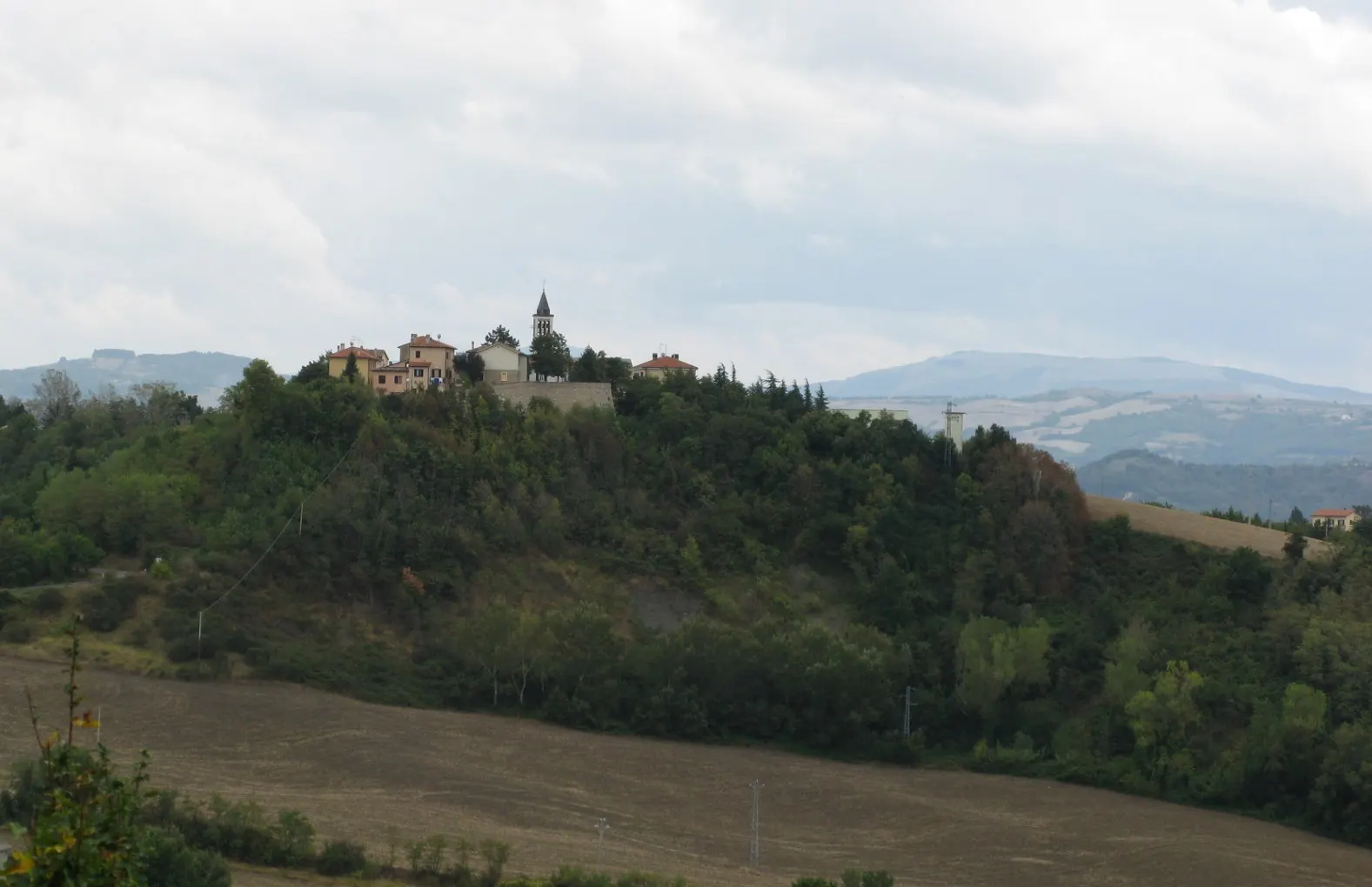 Centro storico di Montecalvo in Foglia su colle verde con campanile e case tra le colline marchigiane