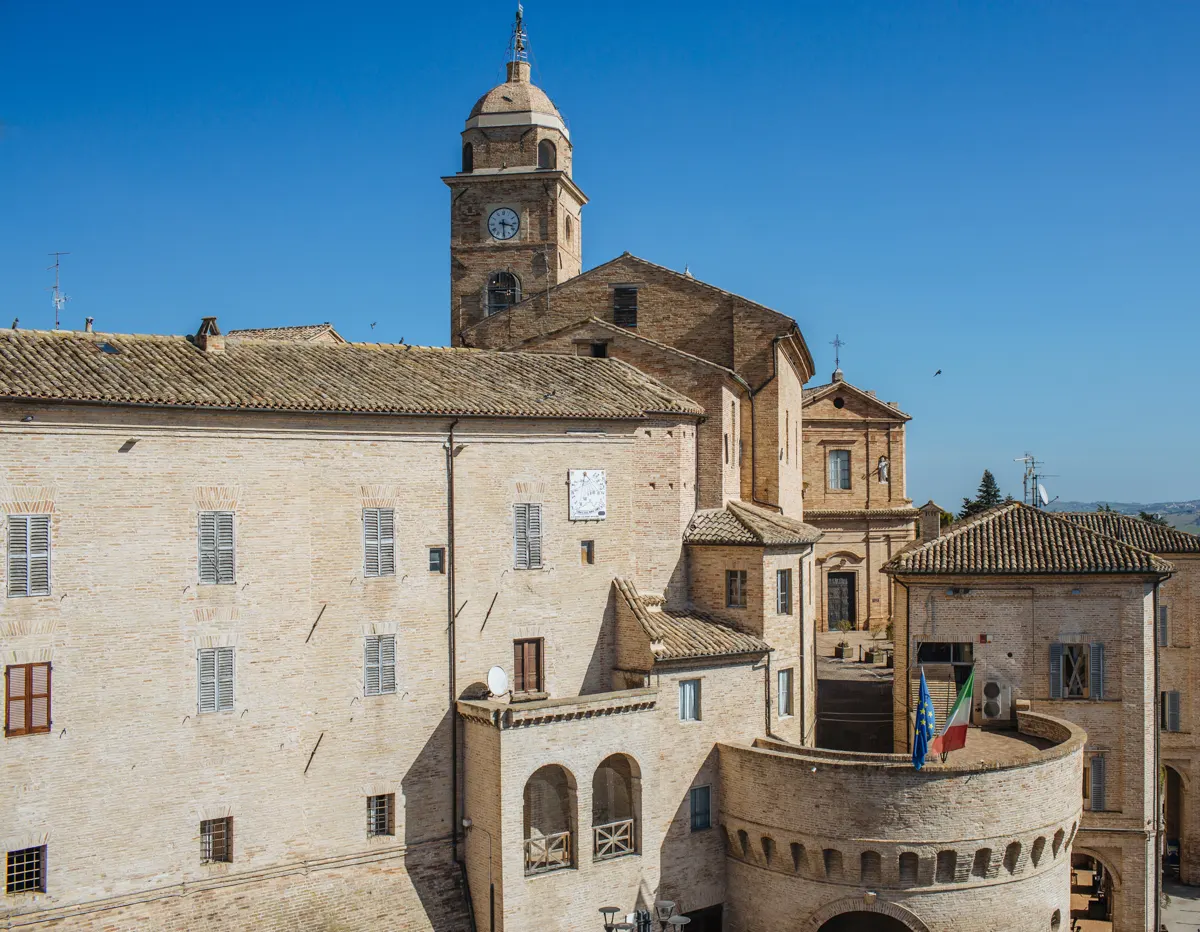 Centro storico di Petriolo con torre campanaria e case in laterizio sotto il cielo azzurro marchigiano