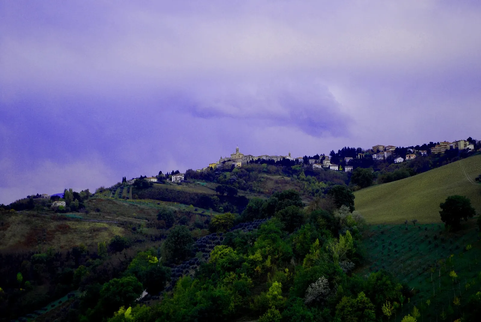 Poggio San Marcello al tramonto su una collina marchigiana circondata da campi coltivati e vegetazione