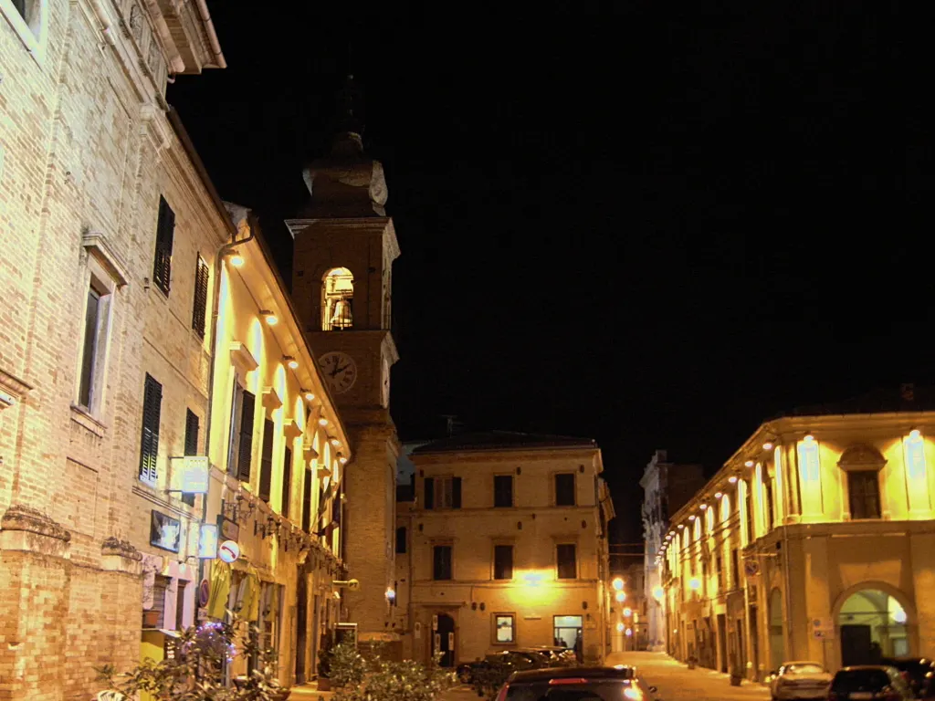 Centro storico di Pollenza illuminato di notte con torre campanaria e palazzi in mattoni nelle Marche