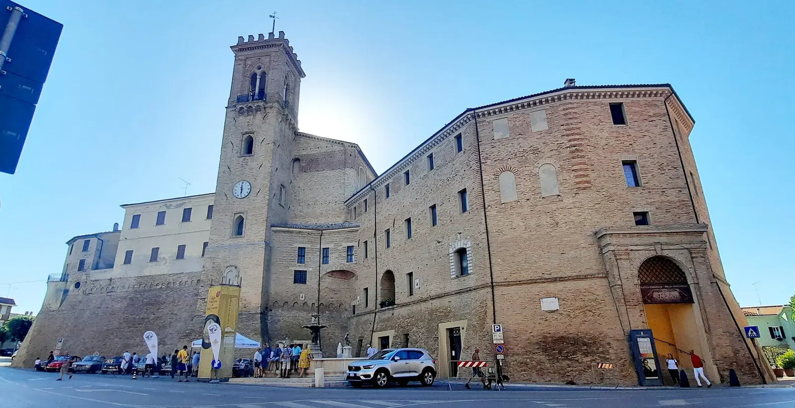 Centro storico di San Costanzo con torre campanaria e palazzi in mattoni sotto cielo azzurro nelle Marche