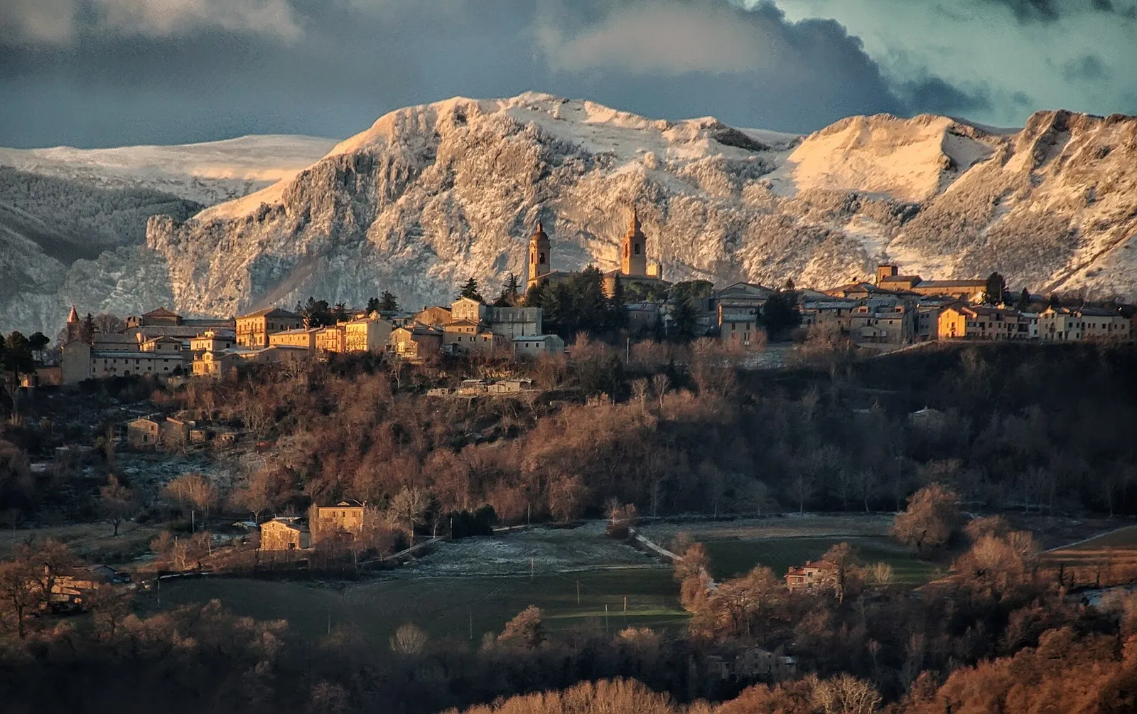 Centro storico di San Ginesio su colle con Monti Sibillini innevati sullo sfondo al tramonto