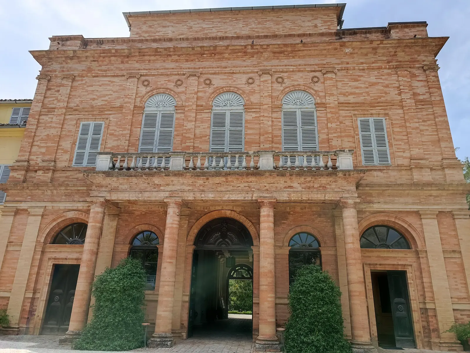 Facciata in mattoni di Palazzo Romani Adami con portici ad arco e finestre con persiane nelle Marche
