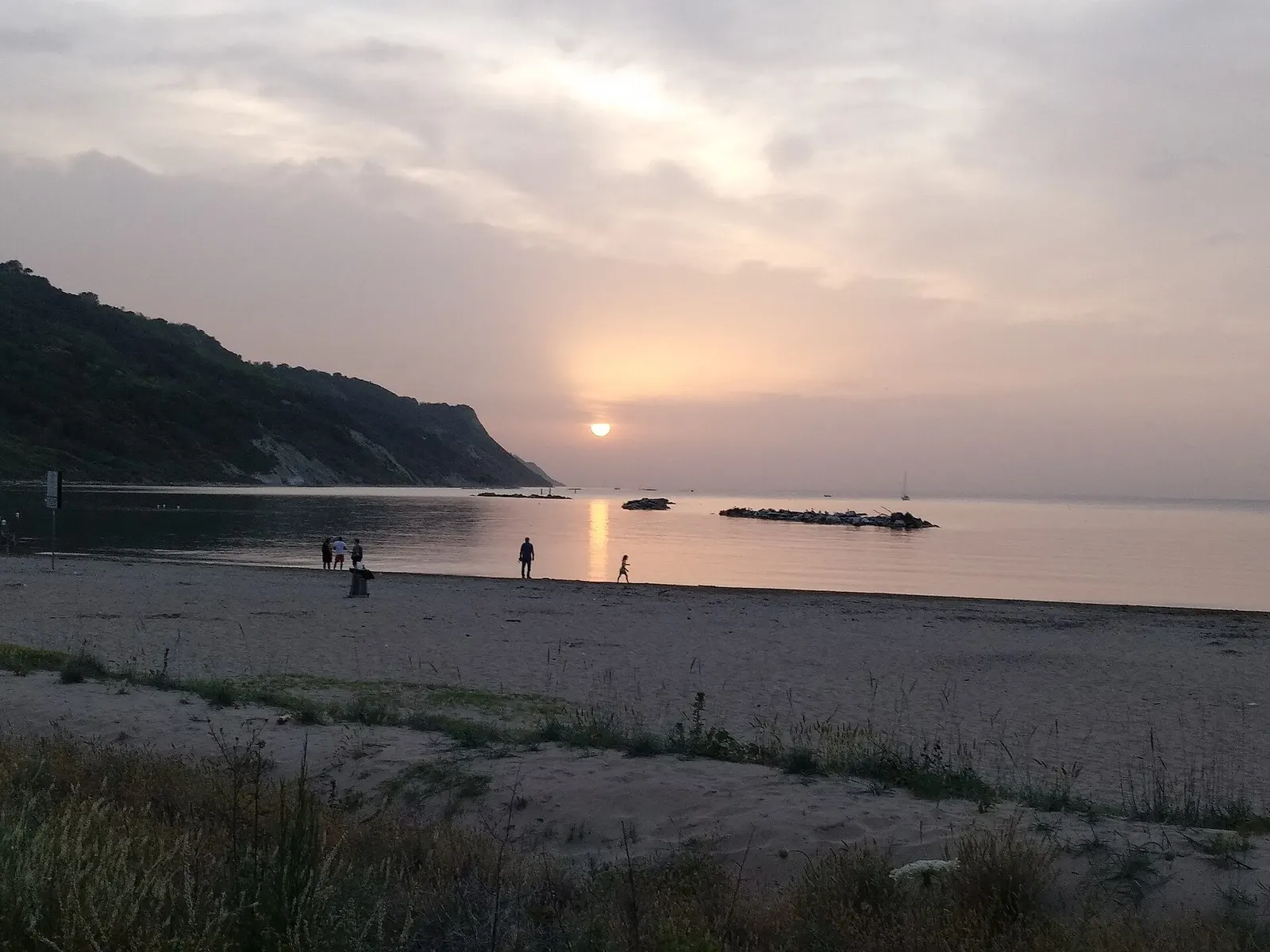 Tramonto sulla spiaggia di Baia Flaminia a Pesaro con mare calmo e promontorio verdeggiante sullo sfondo