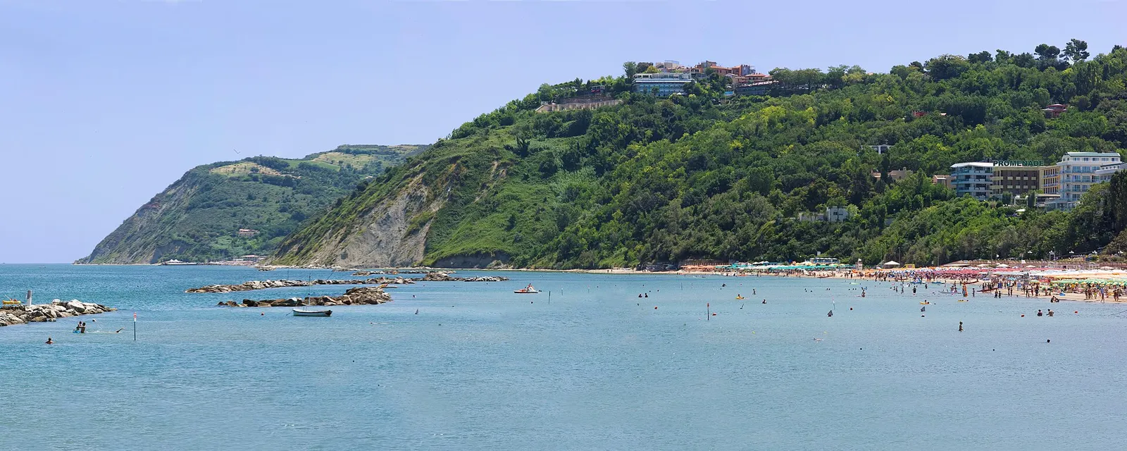 Baia Vallugola con spiaggia affollata tra le verdi colline del Monte San Bartolo a Gabicce Mare