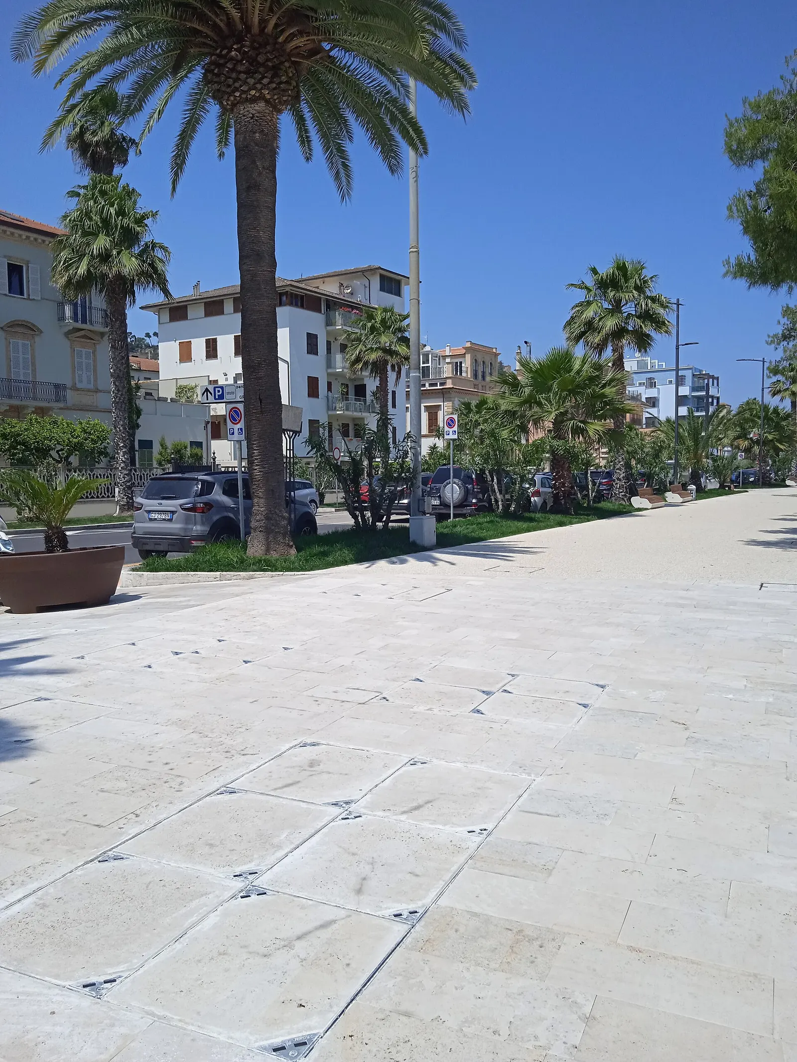 Lungomare di Grottammare con palme e pavimentazione in pietra chiara sotto il sole estivo marchigiano