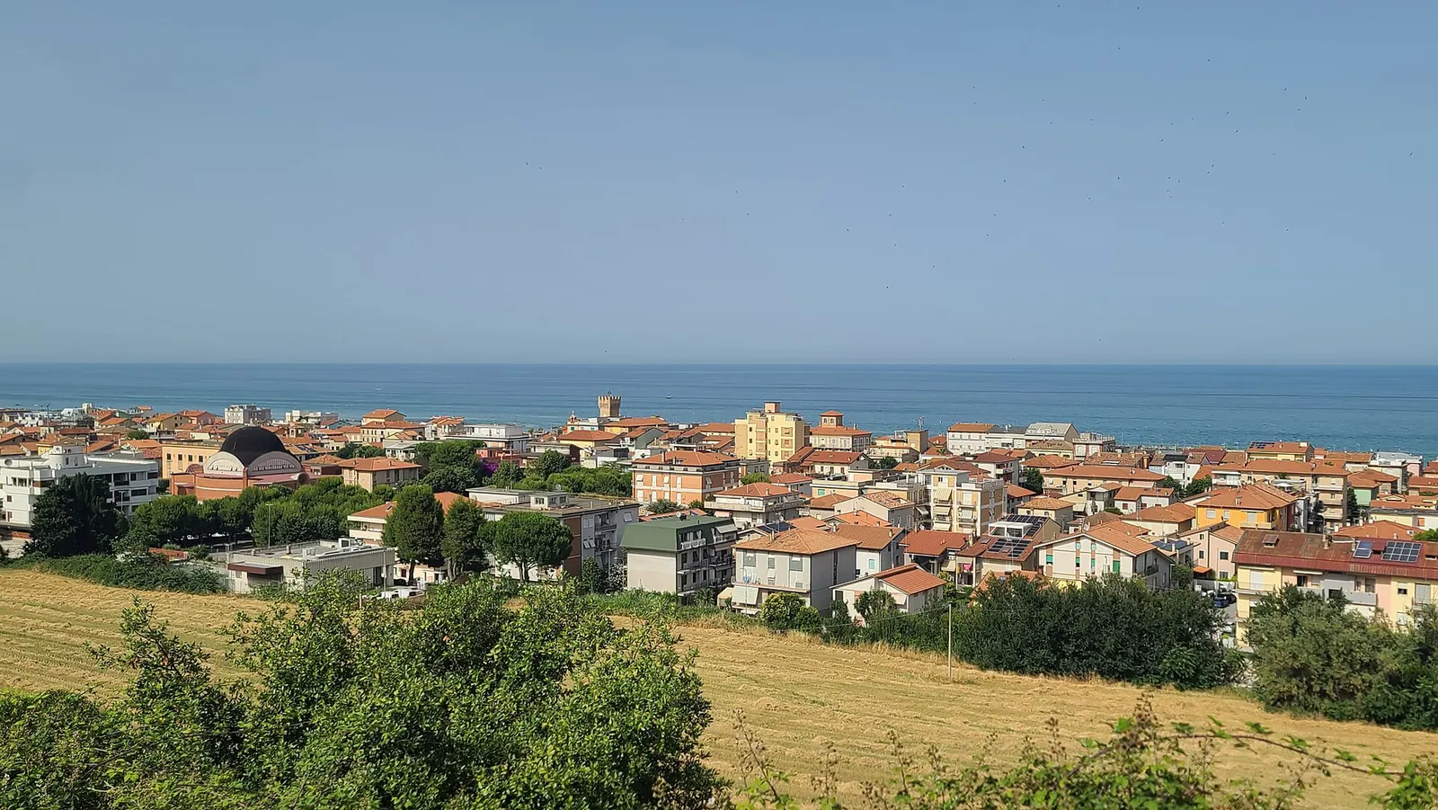 Veduta panoramica di Porto Casimeto con case e tetti colorati tra mare Adriatico e colline verdi marchigiane