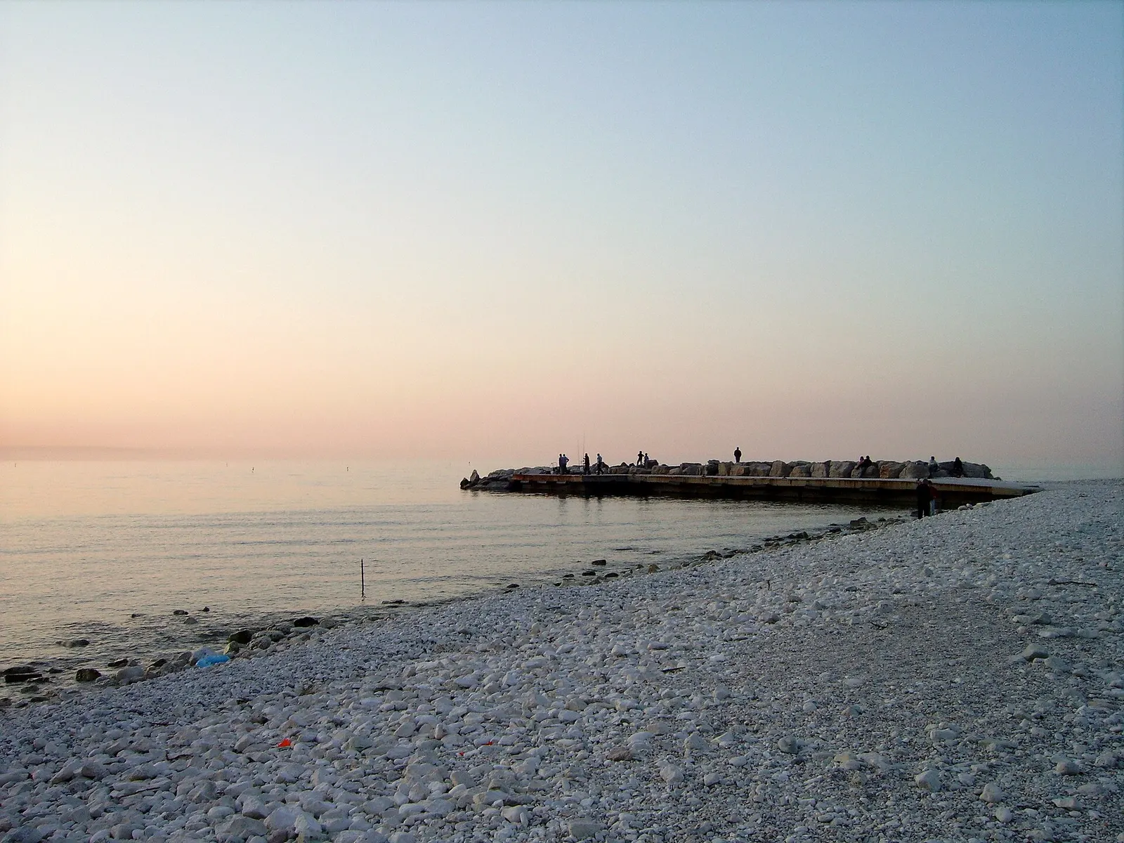 Il molo di Portonovo al tramonto con spiaggia di ciottoli bianchi e mare Adriatico calmo ad Ancona