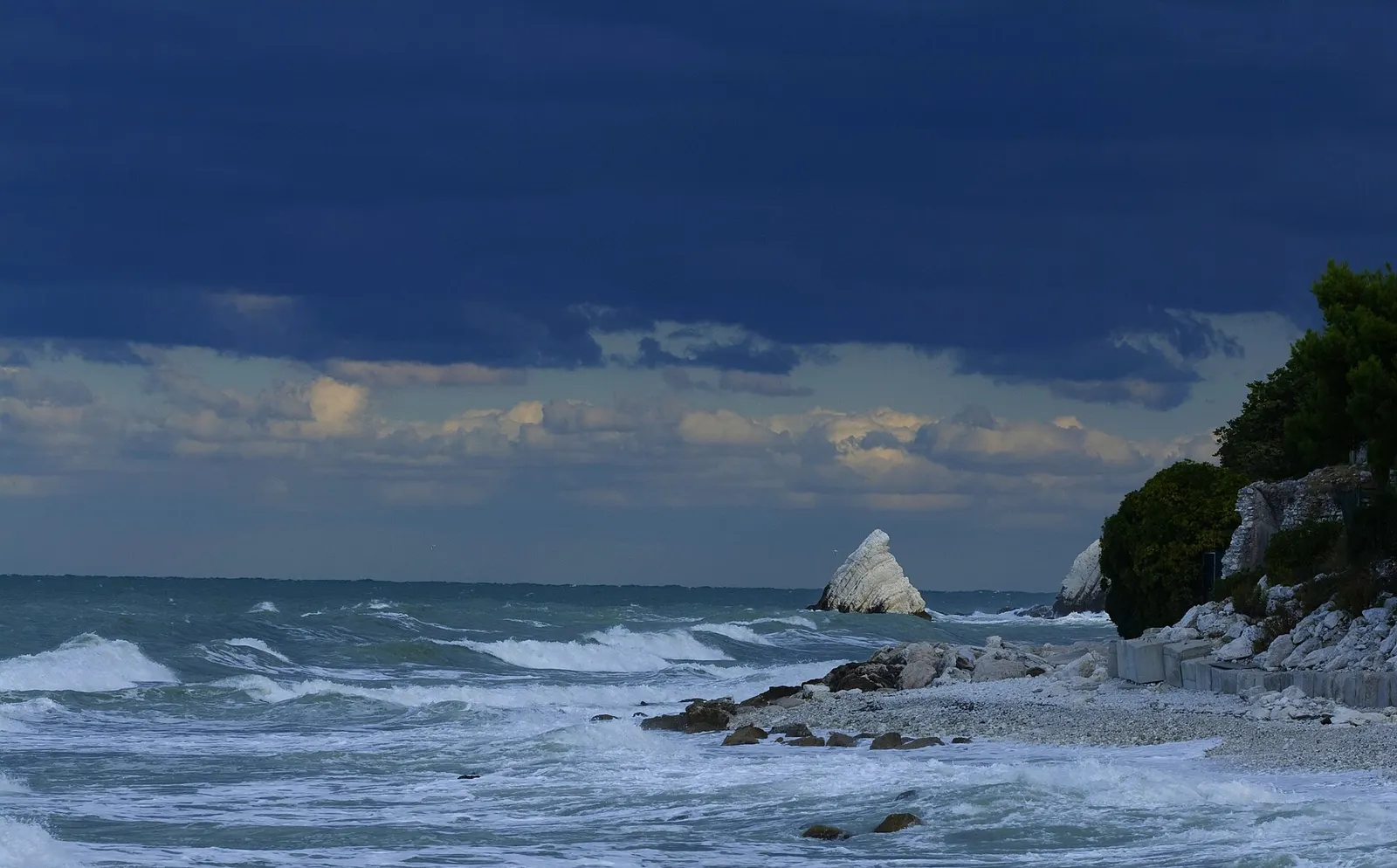 Spiaggia di Portonovo con i due scogli bianchi della Vela emergenti dal mare Adriatico sotto cieli nuvolosi