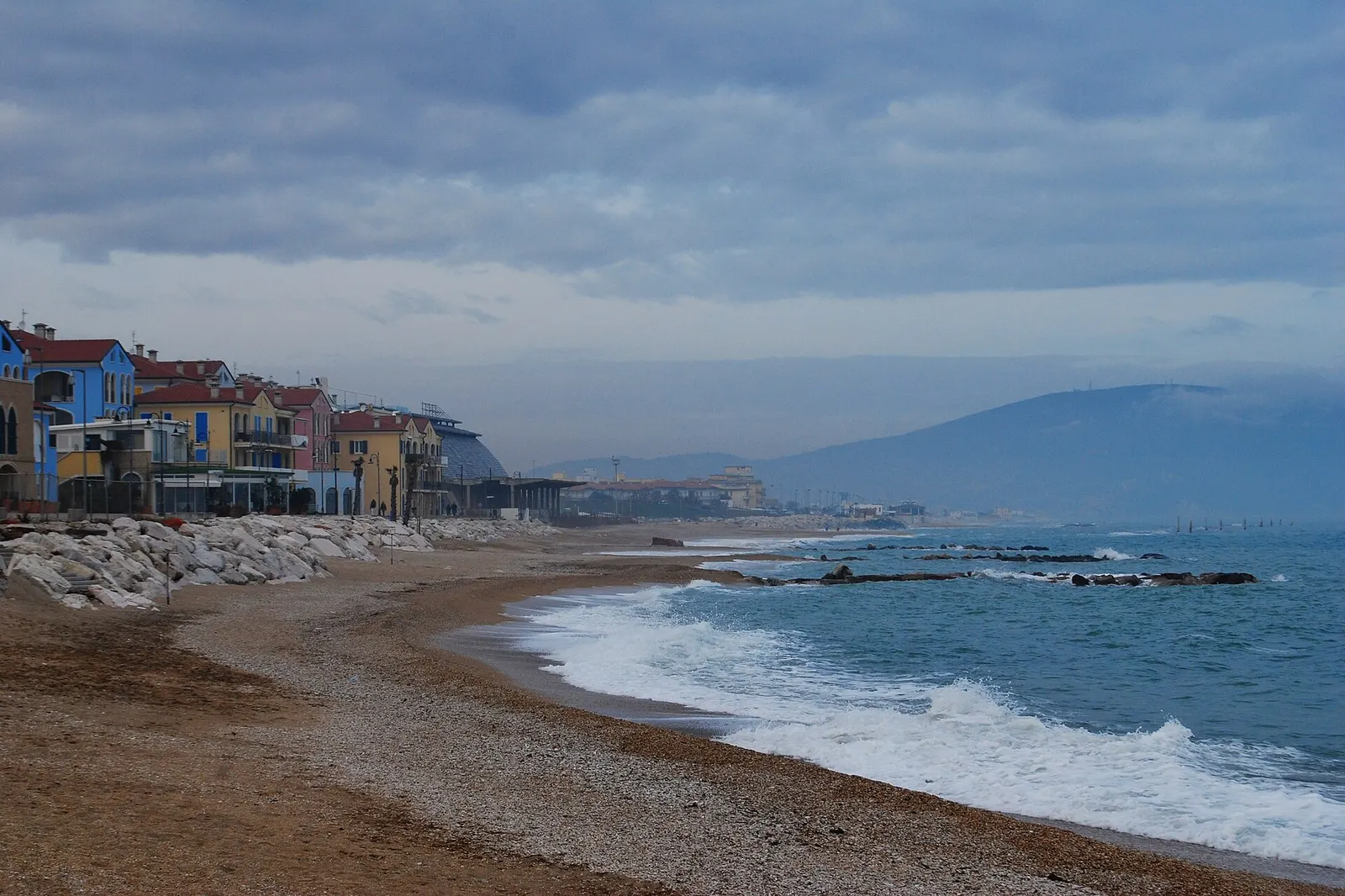 Spiaggia di sabbia e ciottoli con palazzi colorati sul lungomare di Porto Recanati e Monte Conero sullo sfondo