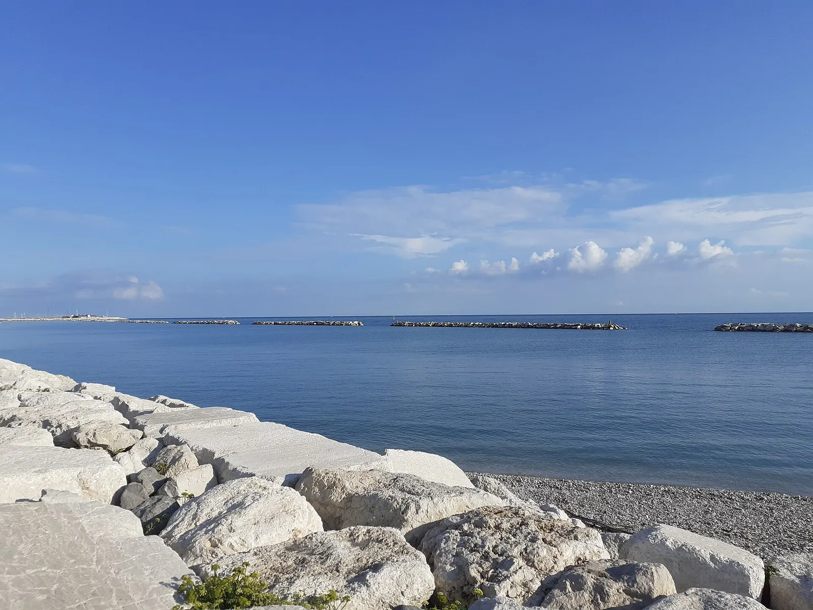 Scogliera bianca e mare calmo con frangiflutti alla Spiaggia di Levante di Fano nelle Marche