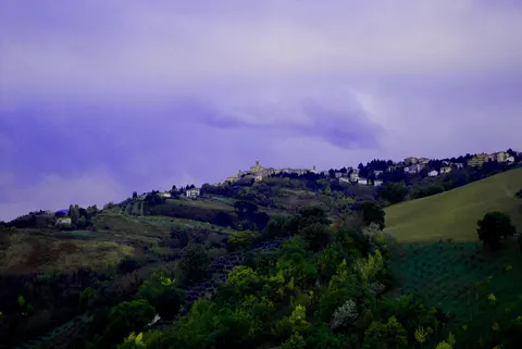 Poggio San Marcello al tramonto su una collina marchigiana circondata da campi coltivati e vegetazione
