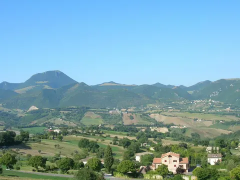 Panorama collinare di Poggio San Vicino con monte sullo sfondo e case sparse tra campi verdi in provincia di Macerata