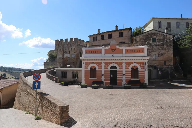 Centro storico di Agugliano con edificio storico rosso e mura merlate sotto cielo azzurro nelle Marche