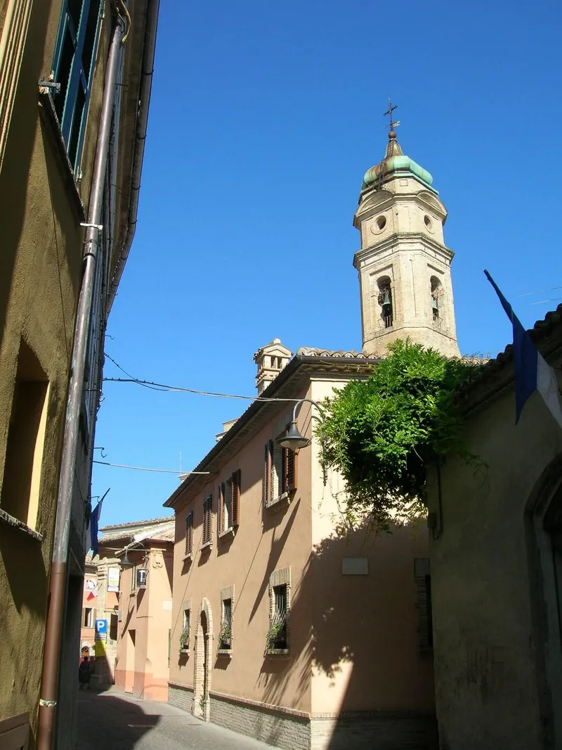 Centro storico di Apiro con campanile della chiesa e vicolo tra case color ocra sotto cielo azzurro